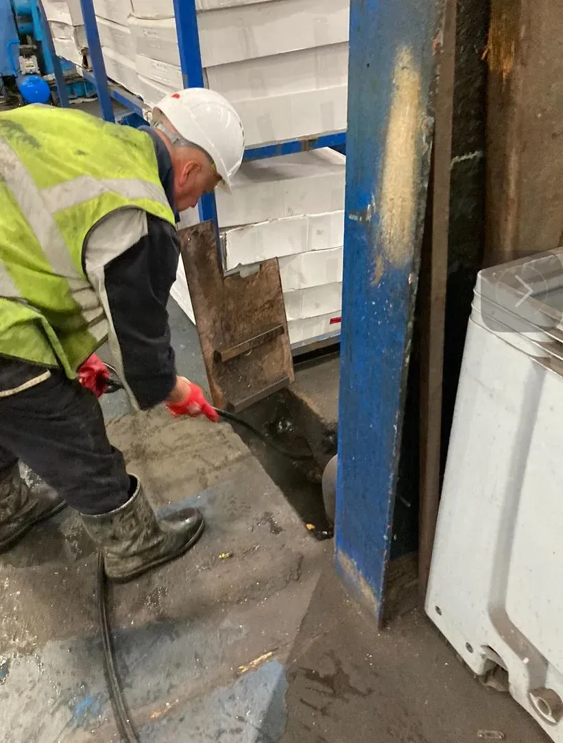 Drainage engineer performing gully cleaning with high-pressure water jetting in a commercial warehouse.
