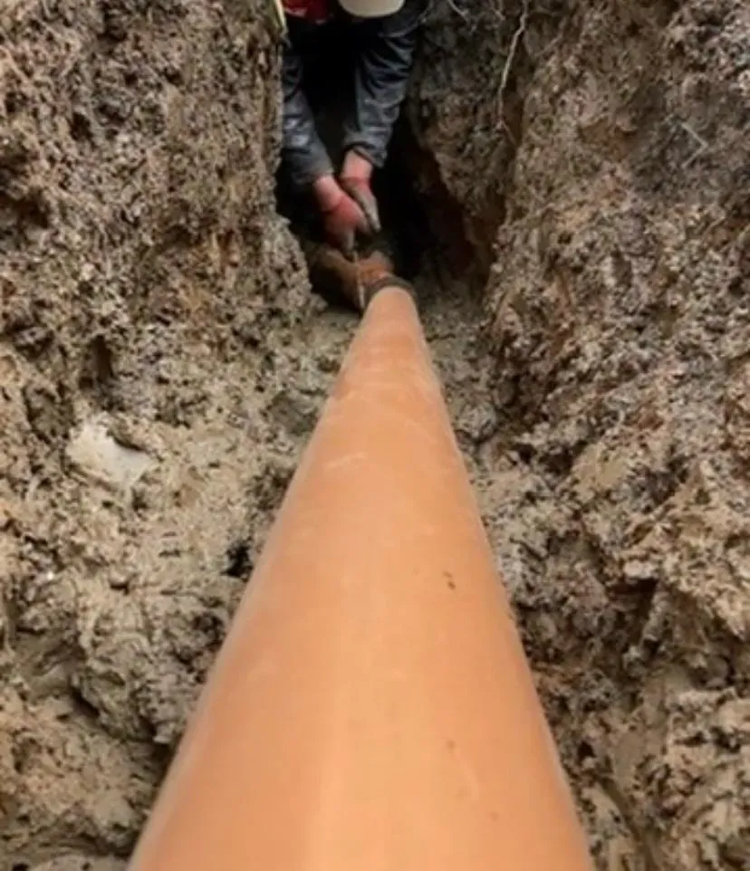 Drainage engineer working on an orange pipe in an excavated trench